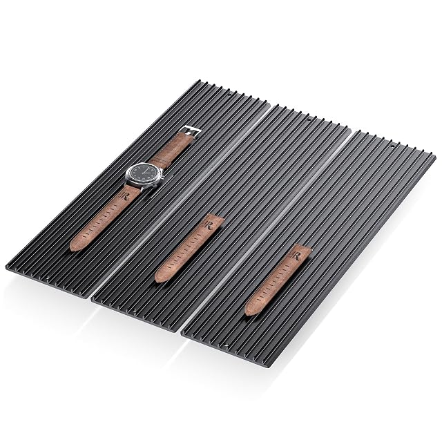 Three black ribbed aluminium slat modules side by side, with a watch and leather straps laid on them